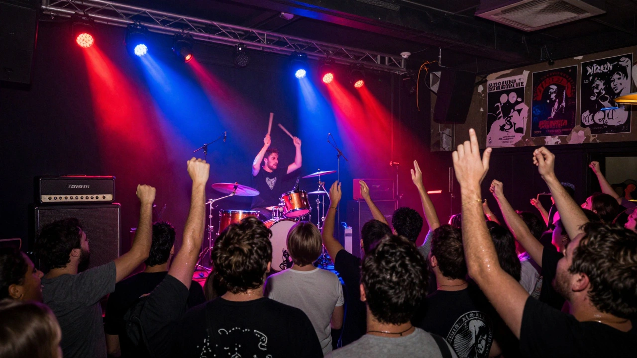 Rock concert crowd surging forward as drummer plays under vibrant stage lights in a historic theatre.